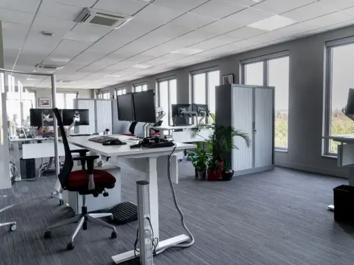 Aménagement moderne de bureaux en open space avec postes de travail équipés de plusieurs écrans, chaises ergonomiques et rangements.