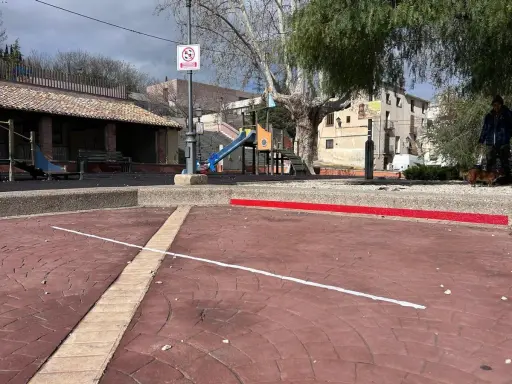 Un parque infantil con toboganes y columpios, evocando los **juegos de antes en la calle**. Un hombre pasea a su perro.