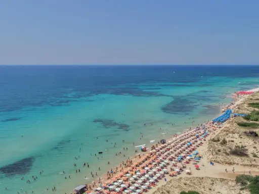 Un tratto di costa con acque cristalline e sabbia dorata, tra le spiaggie più belle del Salento, affollata di ombrelloni e bagnanti.