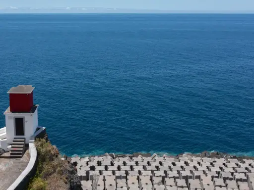 Kleines rotes Haus auf Felsen am Meer bei Ribeira Brava. Wellenbrecher aus Beton säumen die Küste.
