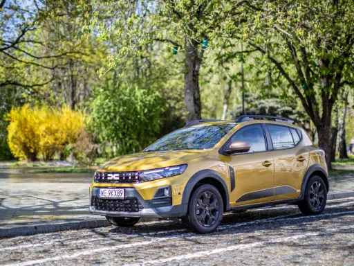 Złoty Dacia Sandero Stepway na tle wiosennej zieleni i kwitnącego krzewu.