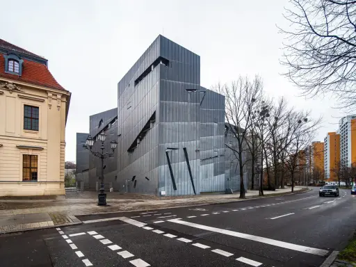 Nowoczesny budynek Muzeum Żydowskiego w Berlinie, obok zabytkowej kamienicy, z charakterystyczną, poszarpaną fasadą.