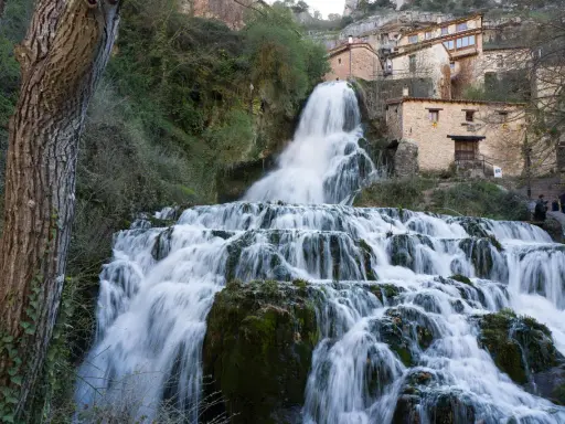 Tosender Wasserfall stürzt über Felsen, Häuser von Orbaneja del Castillo schmiegen sich an den Hang.