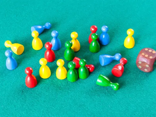 Kolorowe pionki do gry planszowej i drewniana kostka leżą na zielonym polu.