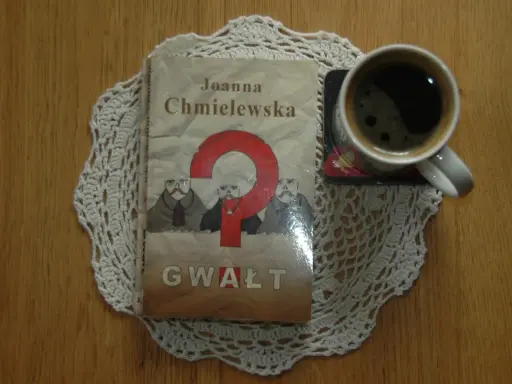 Kawa i książka Joanny Chmielewskiej "Gwałt" na koronkowym obrusie. Idealny zestaw do czytania jej kryminałów chronologicznie.
