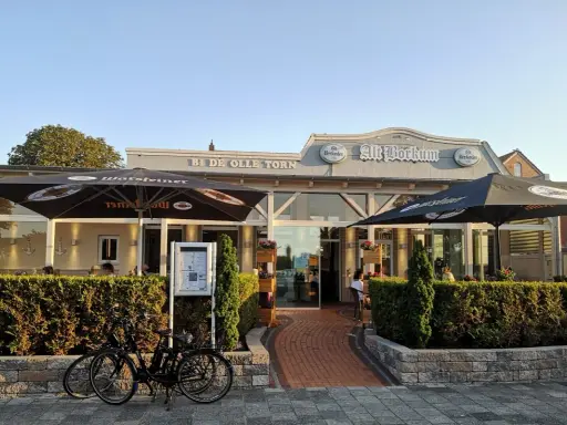 Zwei Fahrräder vor dem Restaurant "Alt Borkum" mit Sonnenschirmen und Büschen.