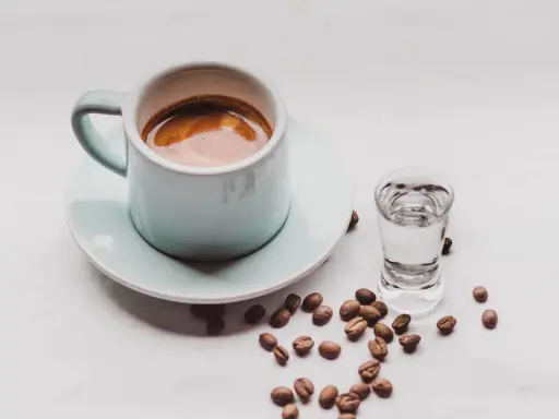 Kawa i alkohol skutki: filiżanka espresso obok kieliszka z wodą i rozsypane ziarna kawy.