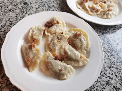Pyszne pierogi z kapustą i grzybami, posypane skwarkami, na białym talerzu.