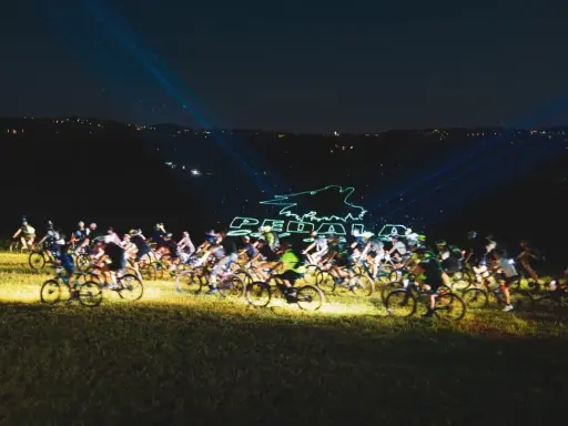 Ciclisti nella notte, illuminati da laser che formano il logo "Pedala coi Lupi". Un'avventura notturna su due ruote.