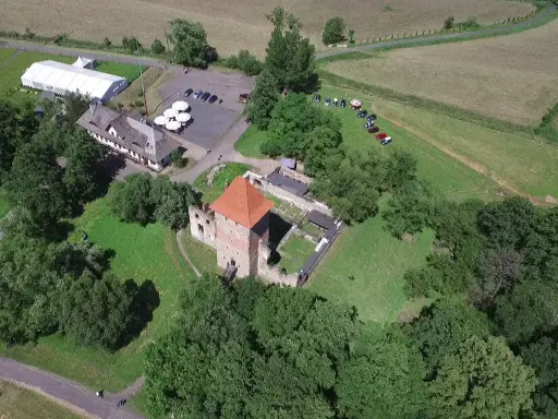 Chudów atrakcje: ruiny zamku z czerwoną wieżą, biały namiot, budynek z drewnianym dachem i parking.