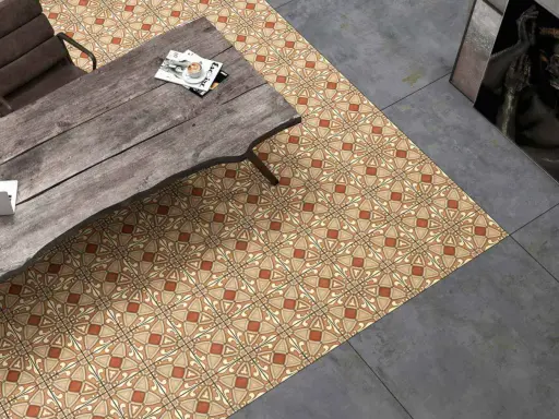Un suelo hidráulico con diseño geométrico en tonos tierra y ocre, junto a un suelo de cemento pulido. Una mesa de madera rústica y una silla completan la escena.