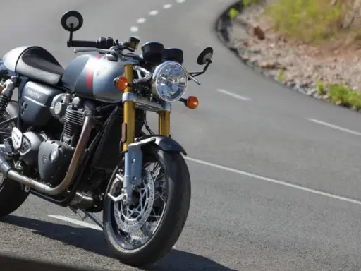Srebrny Triumph Thruxton 900 na krętej drodze, gotowy na triumfalną jazdę.