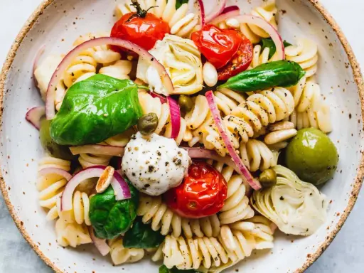 Ein bunter vegetarischer Nudelsalat mit Fusilli, Kirschtomaten, Mozzarella-Kugeln, Artischockenherzen, Oliven und frischem Basilikum.