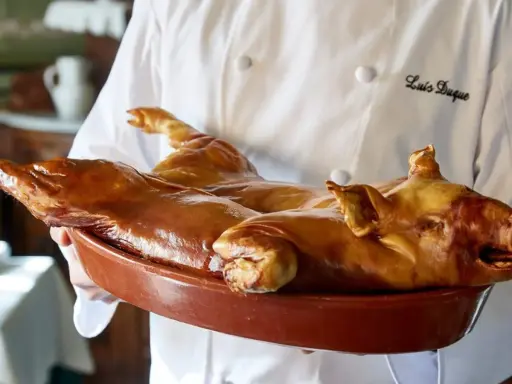 Cochinillo asado, un clásico que comer en Segovia. Un chef presenta este manjar dorado en una cazuela.