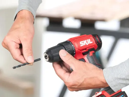 Man insertando una broca en un taladro inalámbrico rojo de la marca SKIL.