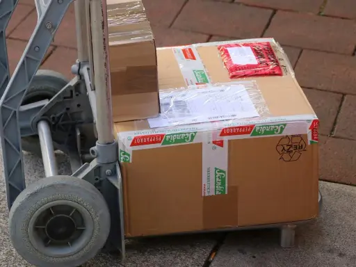 Paczki na wózku, gotowe do wysyłki. Ubezpieczenie paczki DHL to pewność, że dotrze bezpiecznie.