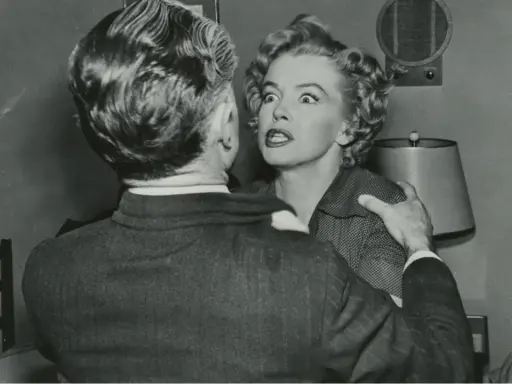 Marilyn Monroe med chockat uttryck i en scen från en av hennes filmer, hon håller fast vid en mans axel.