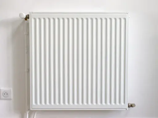 Radiador blanco con termostato, junto a un enchufe. Podría estar haciendo ruido radiador.