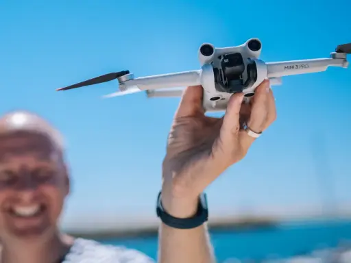 Ręka trzyma drona DJI Mini 3 Pro, gotowego do lotu. Jego imponujący zasięg pozwoli na uchwycenie niesamowitych ujęć.
