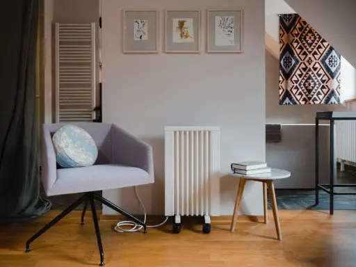 Un fauteuil confortable, un radiateur rayonnant blanc et une petite table avec des livres créent un coin lecture cosy.