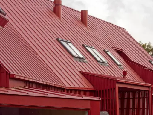 Rött, bandat plåttak med flera takfönster och skorstenar. Ett modernt hus med en slående takkonstruktion.