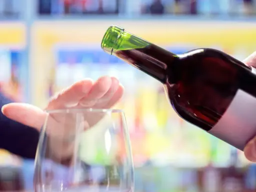 Hand stoppt Weinglas, während eine Flasche Rotwein eingegossen wird. Ein Symbol für bewussten Weinkonsum weltweit.