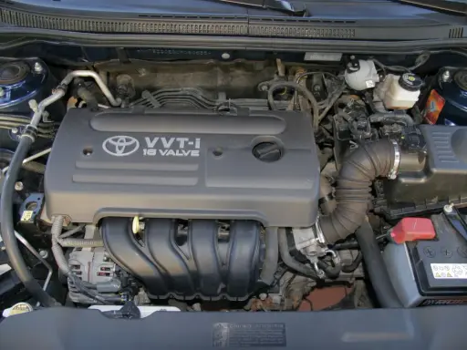 Silnik VVT-i 16 Valve z Toyoty Corolla E12. Widoczny alternator, akumulator i elementy układu dolotowego.