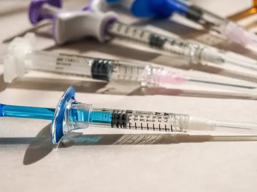 Flera sprutor med blå och lila detaljer ligger på en ljus yta. En spruta med blå kolv är i förgrunden, redo för vaccin i Colombia.