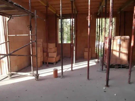 Budowa w toku: szalowanie stropu, rusztowania i materiały budowlane czekają na beton.