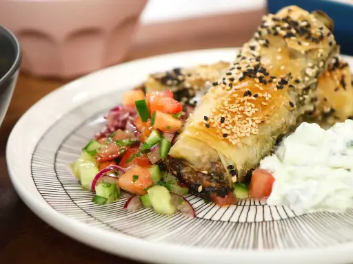 Krispiga filodegsrullar med sesamfrön, serverade med en fräsch tomatsallad och vitlökssås. Ett utsökt burek recept!