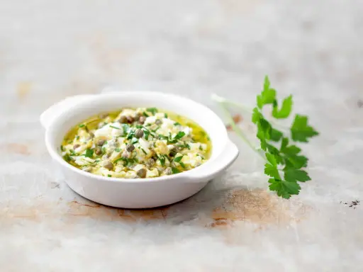 Sauce gribiche, une préparation maison à base d'œufs durs hachés, de câpres et de persil frais, dans un bol blanc.