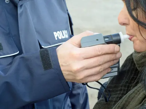 Policjant w mundurze z napisem "POLICJA" mierzy kobiecie poziom alkoholu alkomatem.