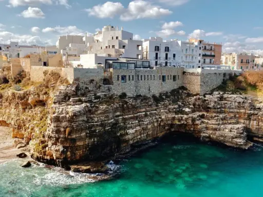 Scogliere mozzafiato e case bianche a picco sul mare turchese, perfetti **posti da visitare in Puglia estate**.