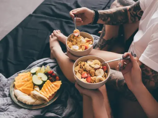 Para jedząca płatki z owocami i talerz świeżych owoców na łóżku. Zdrowy początek dnia, czyli zbilansowana dieta.