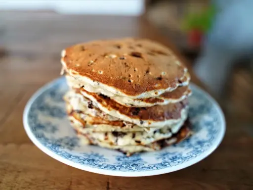 Pile de pancakes pepite chocolat sur une assiette bleue et blanche, prêts à être dégustés.