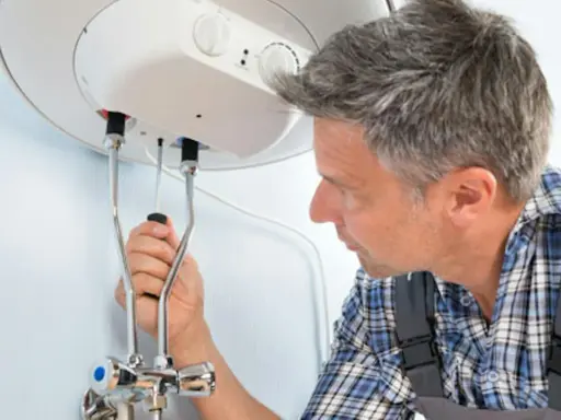 Mann mit Werkzeug am Warmwasserspeicher. Anleitung zum Warmwasserspeicher entkalken.