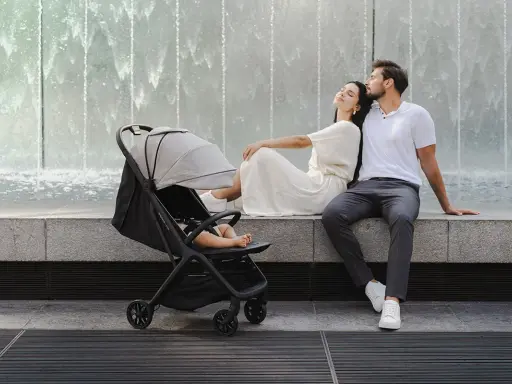 Para spacerówka na leżąco, idealna na rodzinne wycieczki. Para odpoczywa przy fontannie, podczas gdy dziecko śpi w wózku.
