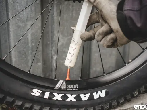 Rękawiczki i strzykawka z mleczkiem uszczelniającym przy wentylu koła rowerowego. Przygotowanie do **prostowania felg rowerowych** i uszczelnienia opony.