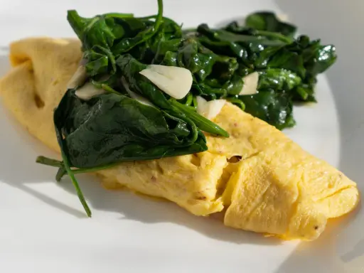 Złożony omlet francuski z zielonym szpinakiem i czosnkiem na białym talerzu.