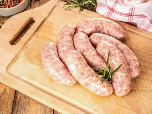 Surowe kiełbaski na desce, obok gałązka rozmarynu. Zastanawiasz się, jak długo można mrozić kiełbasę, by zachowała świeżość?