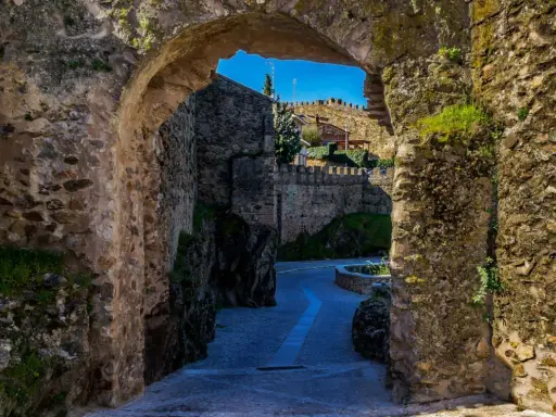 Un arco de piedra revela un camino empedrado y murallas, evocando la atmósfera de pueblos medievales cerca de Madrid.