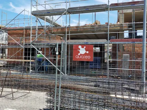 Obra en construcción con andamios y ladrillos. Se ve el logo de "qualee". ¿Cuánto se tarda en construir un edificio de 7 plantas?