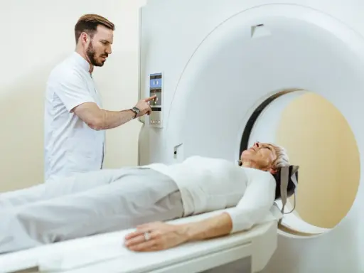 Pacjentka leży na stole do rezonansu magnetycznego, a technik obsługuje konsolę. Czy do rezonansu magnetycznego trzeba się rozebrać? Zazwyczaj tak, aby uniknąć zakłóceń.