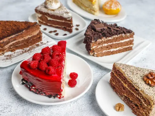 Variedad de pasteles en una mesa: uno de chocolate con cacao, otro con glaseado rojo y frambuesas, y uno con nueces. Una deliciosa carta de postres.