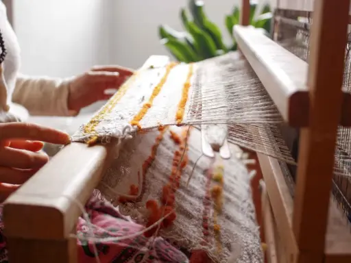 Hands weave a textured fabric on a loom, a beautiful example of textile upcycling.