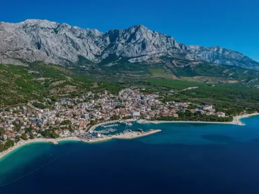 Widok na Baśkę Vodę z górami w tle. Atrakcje turystyczne obejmują plaże, port jachtowy i urokliwe miasteczko.