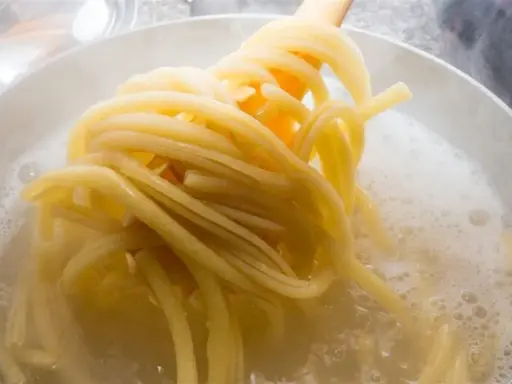 Gorący garnek z bulgoczącą wodą, z którego wyciągane są idealne, sprężyste nitki makaronu al dente.