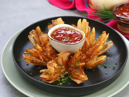 Eine knusprige, blühende Zwiebel, die wie eine Blume aussieht, mit einem Dip in der Mitte.