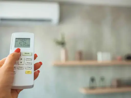 Mano con control remoto ajustando la temperatura ideal aire acondicionado para dormir a 25°C.