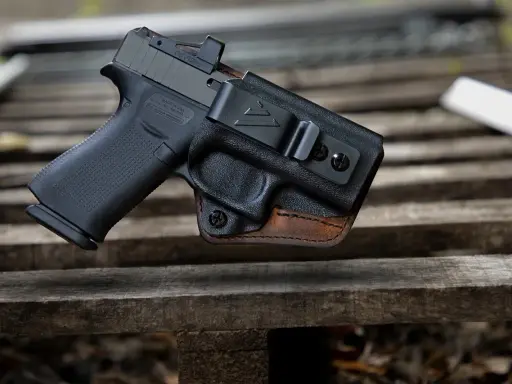 Pistolet w kaburze udowej z czarnego polimeru i brązowej skóry, z widocznym celownikiem optycznym.
